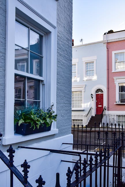 Close-up of a white residential building facade with a decorative railing and a black mailbox installed on the wall beneath it, located at Portobello Road W11 in Notting Hill, London. The surface of t